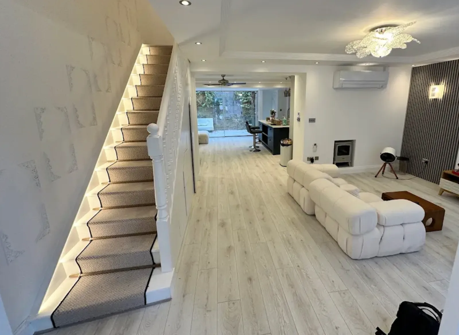 Bright open plan hallway with a carpeted staircase, plank flooring and a living kitchen space beyond