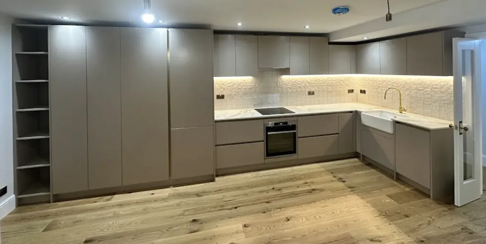 Grey handleless kitchen with marble effect worktops, a Belfast sink, brass tap and integrated appliances